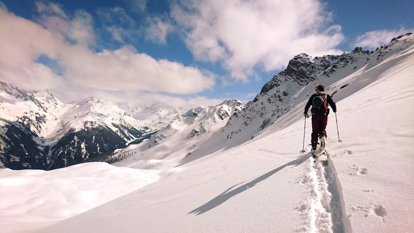 Skitourengeher im Aufstieg über einem verschneiten Grat, dahinter die Gipfel des Montafon