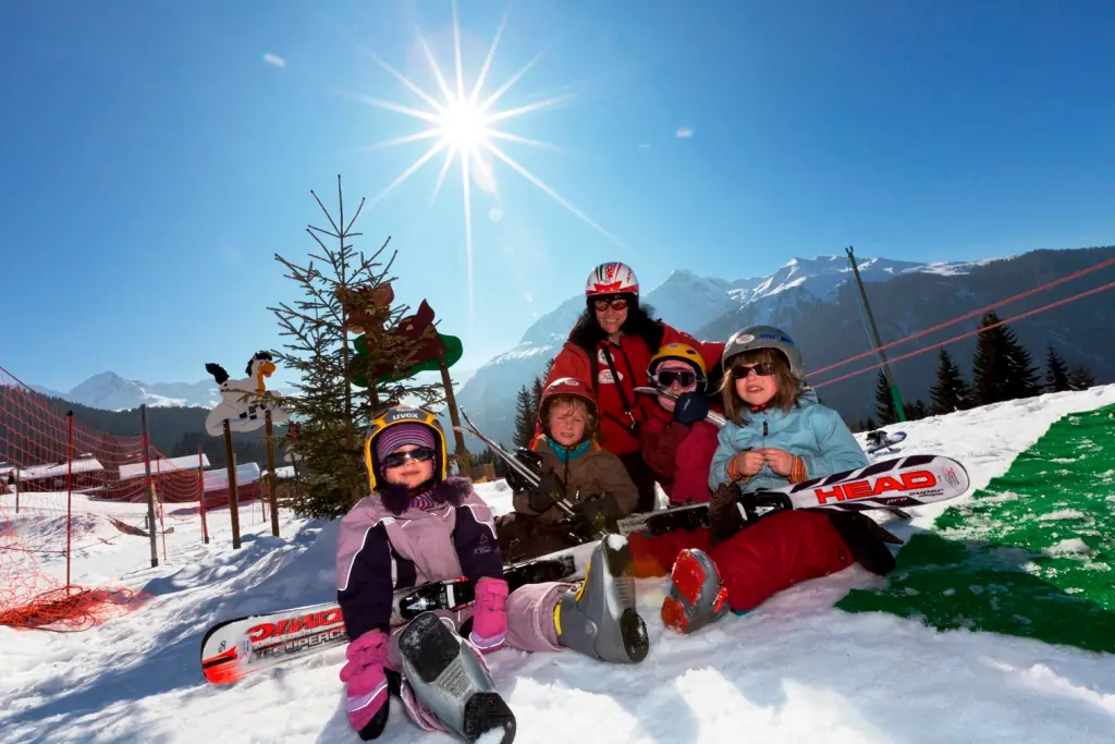 Kinder mit ihren Ski im Skikinderland, dahinter Tannen und Berge