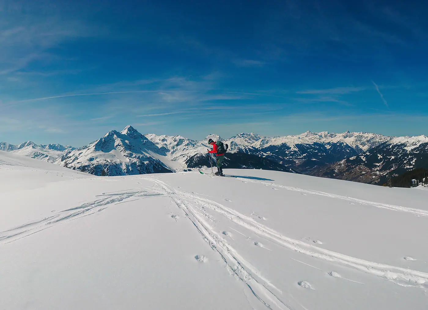 Skitourengeher mit Rucksack auf einem verschneiten Bergrücken, dahinter das Gipfelpanorama